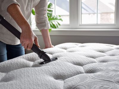 Woman using vacuum cleaner to vacuum mattress in a bedroom Woman using vacuum cleaner to vacuum mattress in a bedroom